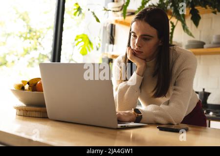 Thoughtful non-binary trans woman using laptop in the kitchen at home Stock Photo