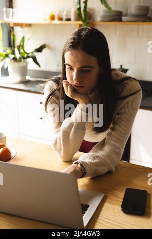 Thoughtful non-binary trans woman using laptop in the kitchen at home Stock Photo
