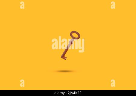 Rusted old metal key floating on a yellow background with shadow and copy space Stock Photo