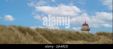 the red top and light of the point of ayr lighthouse peeking over the marram covered sand dunes at talacre beach Stock Photo