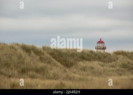 the red top and light of the point of ayr lighthouse peeking over the marram covered sand dunes at talacre beach Stock Photo