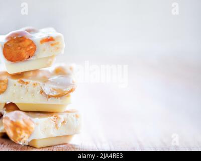 White chocolate with whole hazelnuts on wooden background close up. Few chocolate pieces with whole hazelnuts are stacked. Copy space Stock Photo