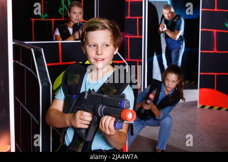 Excited boy aiming laser gun at other players during laser tag game in dark room Stock Photo