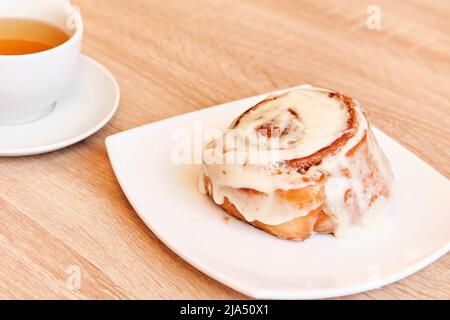 Cinnamon roll with buttercream on white plate and tea in mug Stock Photo