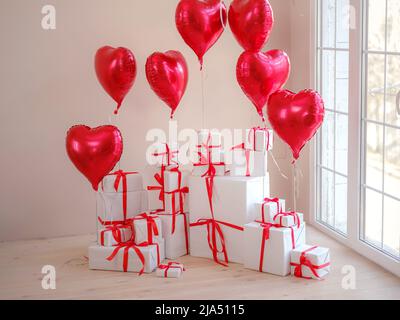 white gift boxes with heart shaped balloons in white living room near window. professional holiday, concept of mother, Valentine's day, birthday. Stock Photo