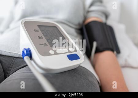 A woman is testing her blood pressure while lying in bed. Stock Photo