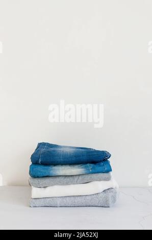 Stack of sweaters  and  blue jeans on grey background, ironing, laundry, home comfort, textile, knitted, women's clothing, cotton, women's casual all- Stock Photo