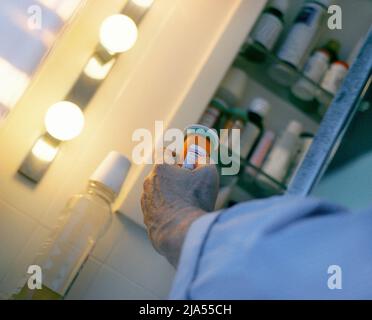 Man taking medication. Open medicine cabinet. Senior reading label on pill bottle before medicating. Medical treatment health. Pharmaceutical industry Stock Photo