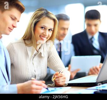 Smiling businesswoman posing while colleagues talking together in bright office Stock Photo