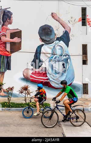Two Cyclists Passing By A Colourful Wall Mural In The Barranco District, Lima, Peru. Stock Photo