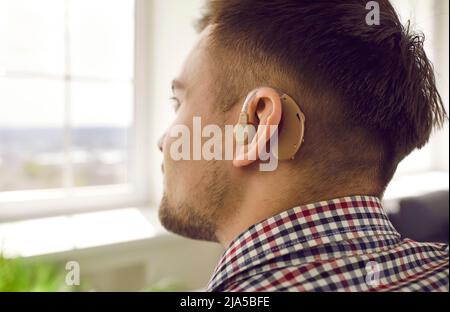 Close up shot of young man who has lost his hearing wearing hearing aid on his ear Stock Photo