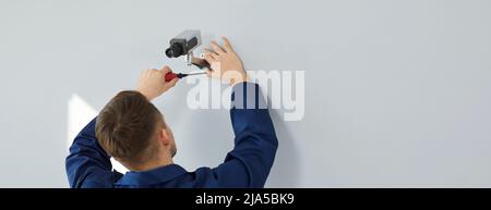 Electrician installing modern surveillance CCTV camera on wall inside the building Stock Photo