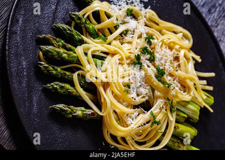 roasted asparagus spears with pasta sprinkled with shredded pecorino cheese and parsley on black plate on dark wood table, close-up Stock Photo