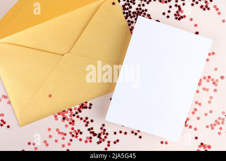 Invitation card mockup with golden envelope and white empty paper and red star shaped confetti Stock Photo
