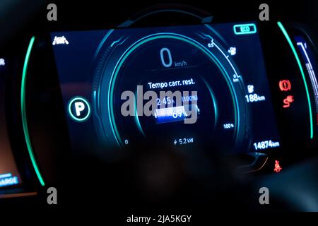 Electric car digital speedometer dashboard on charge in Portuguese Language, displaying the word ' Remaining charging time '. Stock Photo