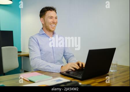 Positive businessman typing on laptop in coworking space Stock Photo