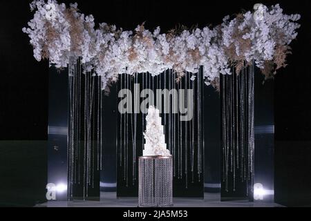 Night wedding ceremony, the arch is decorated with flowers, candles and garlands and there is a wedding cake on the table Stock Photo