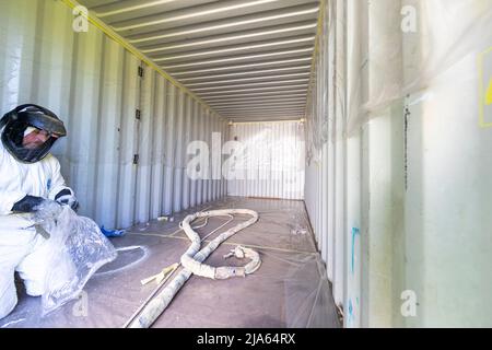 A workman sprays a shipping container ceiling with Grapho Therm to prevent the build up of condensation. Stock Photo