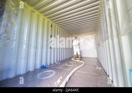 A workman sprays a shipping container ceiling with Grapho Therm to prevent the build up of condensation. Stock Photo