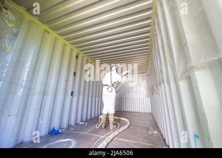 A workman sprays a shipping container ceiling with Grapho Therm to prevent the build up of condensation. Stock Photo