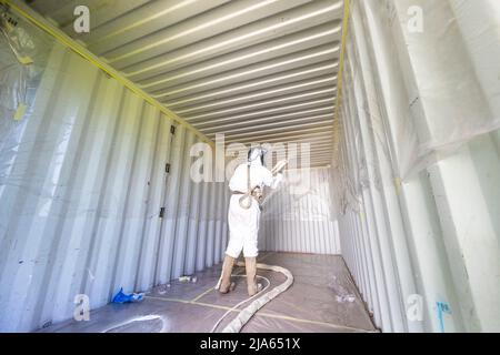 A workman sprays a shipping container ceiling with Grapho Therm to prevent the build up of condensation. Stock Photo