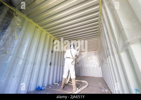 A workman sprays a shipping container ceiling with Grapho Therm to prevent the build up of condensation. Stock Photo