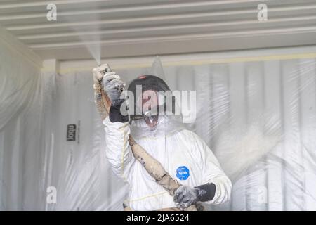 A workman sprays a shipping container ceiling with Grapho Therm to prevent the build up of condensation. Stock Photo