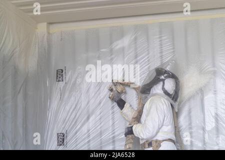 A workman sprays a shipping container ceiling with Grapho Therm to prevent the build up of condensation. Stock Photo