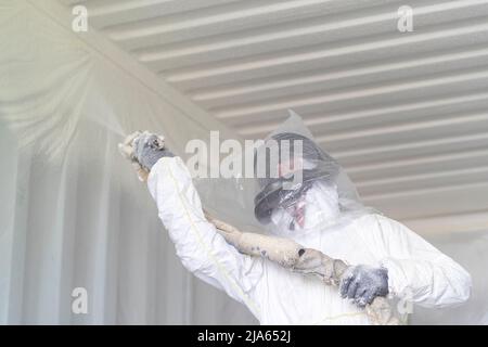 A workman sprays a shipping container ceiling with Grapho Therm to prevent the build up of condensation. Stock Photo