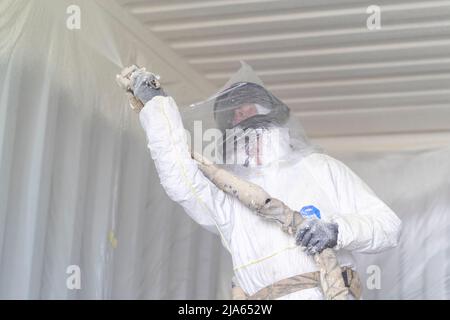 A workman sprays a shipping container ceiling with Grapho Therm to prevent the build up of condensation. Stock Photo