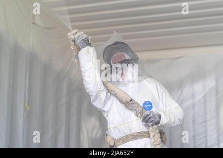 A workman sprays a shipping container ceiling with Grapho Therm to prevent the build up of condensation. Stock Photo