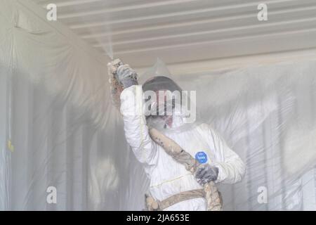 A workman sprays a shipping container ceiling with Grapho Therm to prevent the build up of condensation. Stock Photo