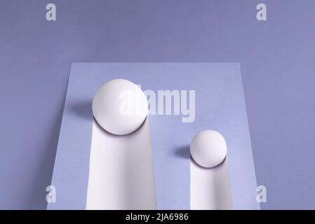 Two white balls roll downhill and leave a trail on a purple background. Abstract minimal concept. Isometric rectangle with copy space. Geometric shape Stock Photo