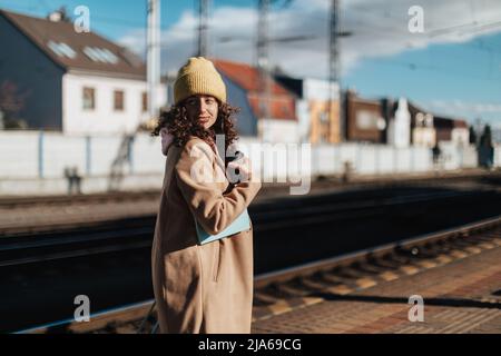 Happy young traveler woman with cup of coffee at train station platform Stock Photo