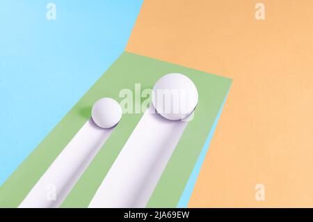 Two white balls roll downhill and leave a trail on a multicolor background. Abstract minimal concept. Isometric rectangle with copy space. Geometric s Stock Photo