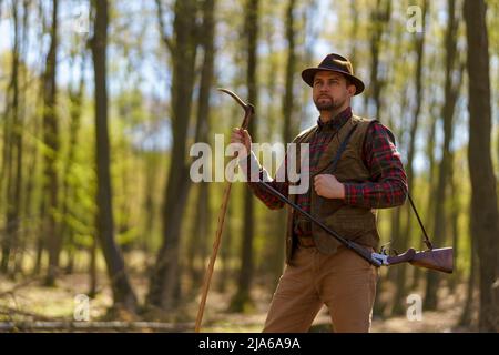Hunter man with rifle gun on hunt in forest. Stock Photo