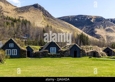 Traditional Icelandic turf-roofed houses stand here in the open-air section of the Skógar Museum (Skógasafn) near Skógar, in front of wooded slopes and a distinctive mountain ridge. Founded in 1949 by local historian Þórður Tómasson, the museum today comprises three sub-museums and six historic buildings housing around 18,000 exhibits on the history of southern Iceland. Stock Photo