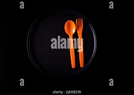 Orange plastic fork and knife on a black plate, isolated on a black background, top view Stock Photo