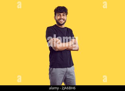 Happy handsome young Indian man in casual clothes standing isolated on yellow background Stock Photo