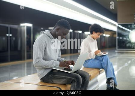 young people using their devices while sitting on a bench in the Stock Photo