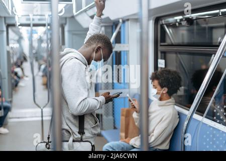 passengers in protective masks using their devices in the subway car . Stock Photo