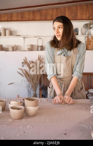 Master of art ceramics at work happy woman in an apron works in a ceramic workshop. The craftswoman creates handmade dishes in the workshop. The Stock Photo