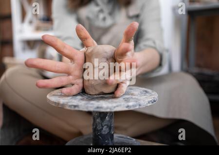 A woman works on a potter's wheel. An artisan molds a cup from a clay pot. Workshop of hand molding. Stock Photo