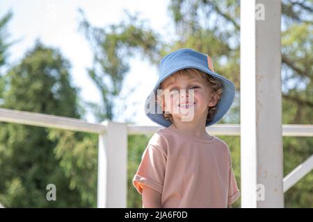 boy standing in the park.a curly-haired boy of five years stands smiling in a green park Stock Photo