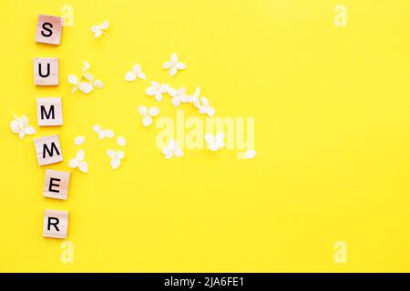 Word summer written from a wooden cubes with letters on a yellow background with a petals of a hydrangea flowers Stock Photo