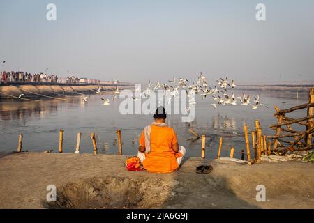 A pilgrim meditates on the bank of the Ganges river during the Kumbh Mela festival. Every twelve years, millions of Hindu devotees begin a massive pilgrimage to the most sacred of Indian festivals: the Kumbha Mela, which takes place in Prayagraj, a place considered particularly auspicious because it is at the confluence of the Ganges, Yamuna and the mythical Saraswati. It is estimated that in 2019, 120 million people attended the sacred enclosure over the course of a month and a half. These numbers, equivalent to the total population of Japan, and 40 times the number of pilgrims who visit Mecc Stock Photo