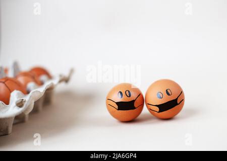 chicken eggs with drawn medical mask with egg carton on a white background. Easter eggs holidays decoration. Stock Photo
