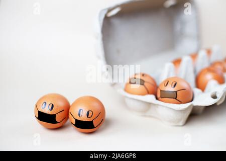chicken eggs with drawn medical mask with egg carton on a white background. Easter eggs holidays decoration. Stock Photo