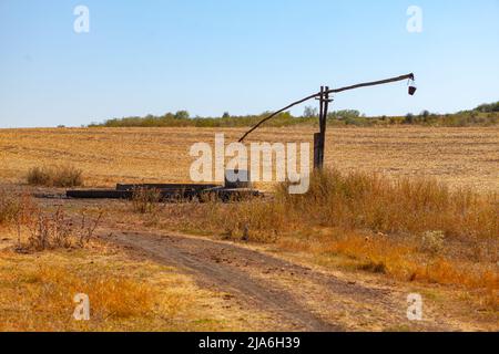 Ancient well with old lifting mechanism of water . Agriculture field in summer Stock Photo