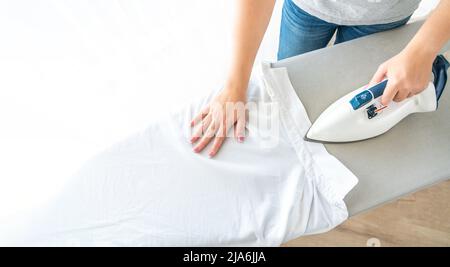 Female hands ironing white shirt collar on ironing board, view from above with copy space Stock Photo